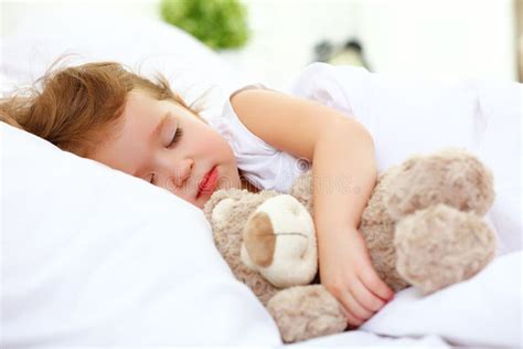 La Petite Fille D Enfant Dort Dans Le Lit Avec L Ours De Nounours Photo