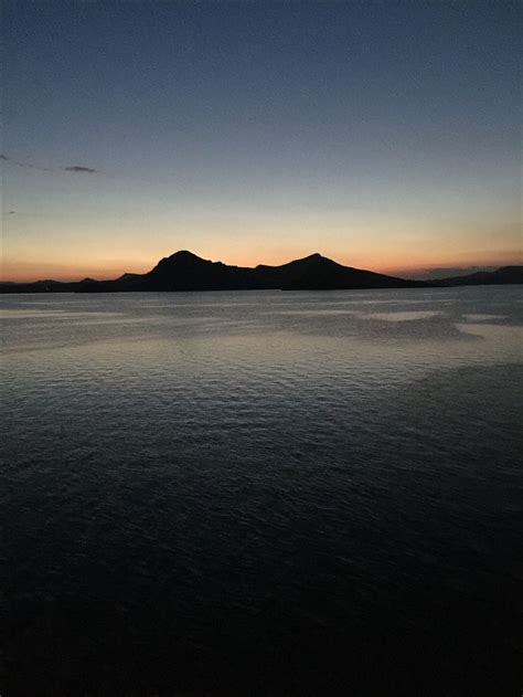 The Sun Is Setting Over Water With Mountains In The Distance