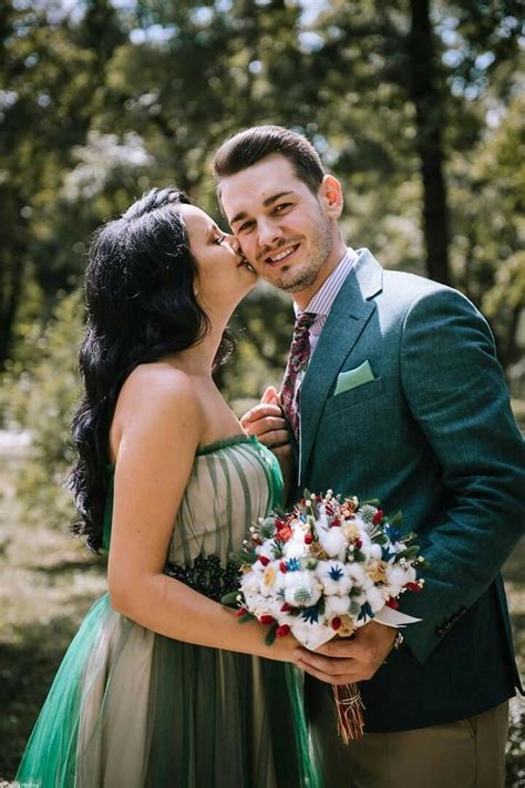 A Man In A Suit And Tie Kissing A Woman Wearing A Green Dress With Flowers