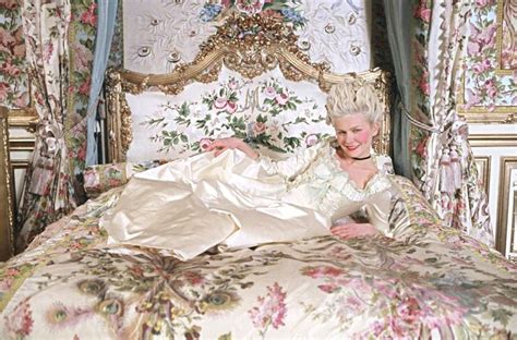 A Woman Laying On Top Of A Bed In A Room With Floral Walls And Curtains