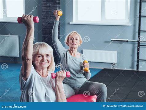 Two Elderly Ladies Lifting Weights While Training In Gym Stock Image