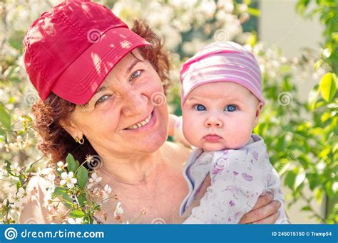 Grandmother Holds Her Little Granddaughter In Her Arms In A Blooming