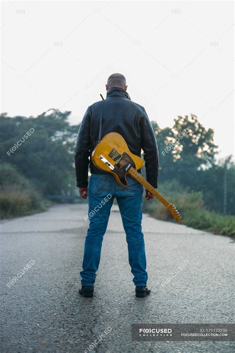 Back View Of Adult Man Carrying Electric Guitar On Standing On Empty