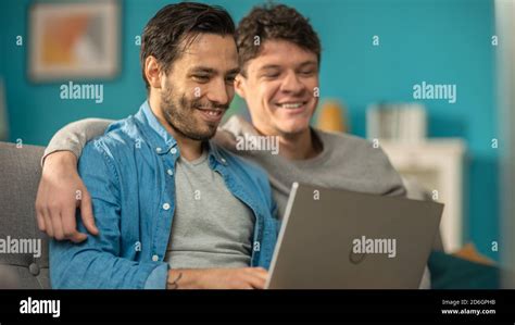 Adorable Male Gay Couple Spend Time At Home They Sit On A Sofa And Use The Laptop They Watch