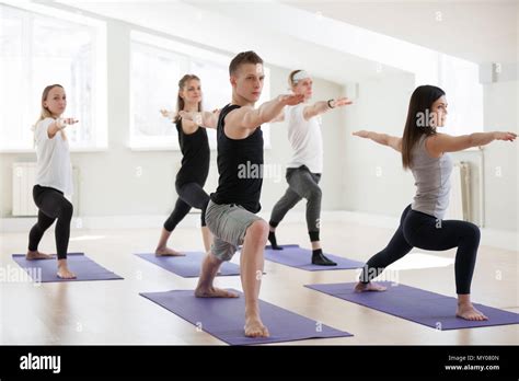 Group Of Young Sporty People Practicing Yoga Lesson Doing Warrior Two