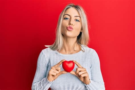 Schöne blonde Frau mit Herz in Kamera schaut und einen Kuss bläst der schön und sexy