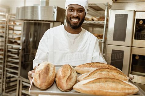 Handsome African American Baker With Tray Of Fresh Loaves Of Bread On