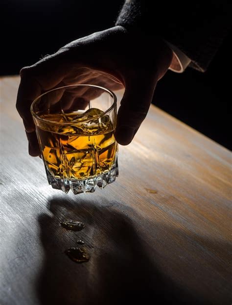 Premium Photo Man S Hand Holding A Glass Of Whisky Over A Table In A