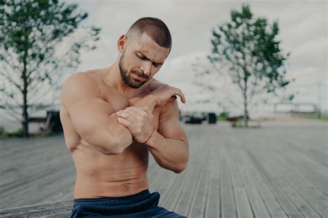 Outdoor Shot Of Muscular Guy Injured Elbow During Physical Exercises