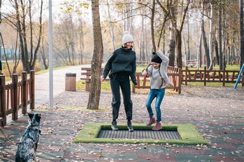 Mom And Her Daughter Jumping Together On Trampoline In Autumn Park