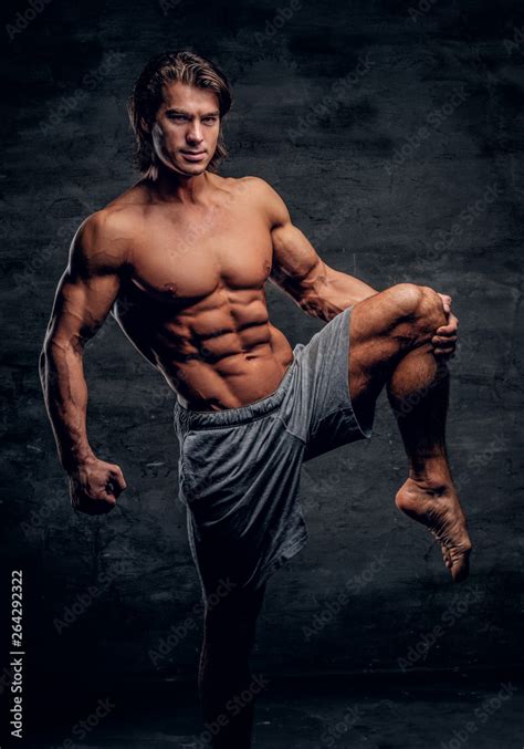 Smiling Attractive Bodybuilder With Naked Torso Is Doing Leg Strechening On Grey Background