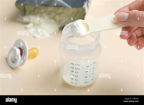 Woman preparing infant formula on beige background, closeup. Baby milk