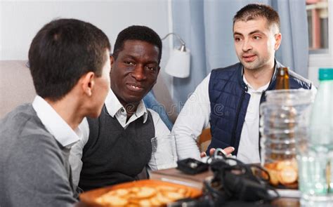 Three Cheerful Men Talking And Laughing While Drinking Beer At Home