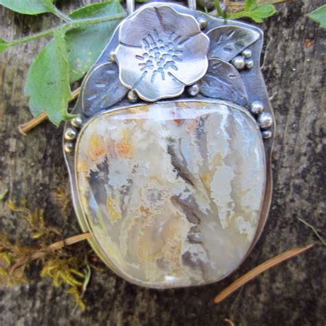 A Silver Pendant With A Flower On It Sitting On Top Of A Tree Trunk