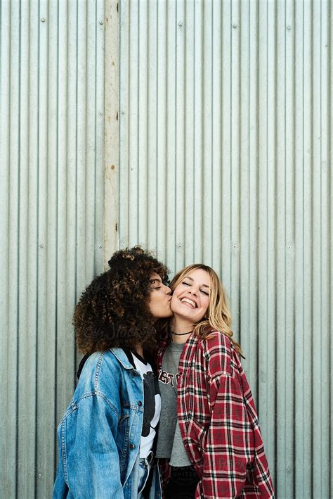 Happy Diverse Girlfriends Kissing Against Metal Wall By Stocksy