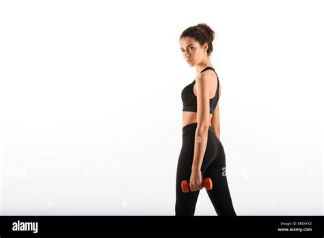 Side View Of Calm Curly Brunette Fitness Woman Holding Dumbbells And Looking At The Camera Over