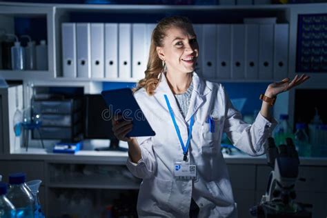 Beautiful Blonde Woman Working At Scientist Laboratory Late At Night Pointing Aside With Hands