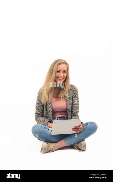 Belle fille blonde européenne assise avec des jambes croisées sur le sol riant et tenant un