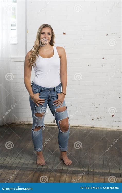 La Jeune Femme Blonde Sexy Pose Dans Le Haut De La Cuve Blanc Et Des Jeans Déchirés Photo stock