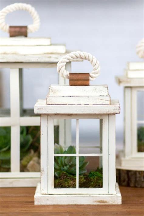 Two White Lanterns With Rope Handles And Windows On Top Of A Wooden