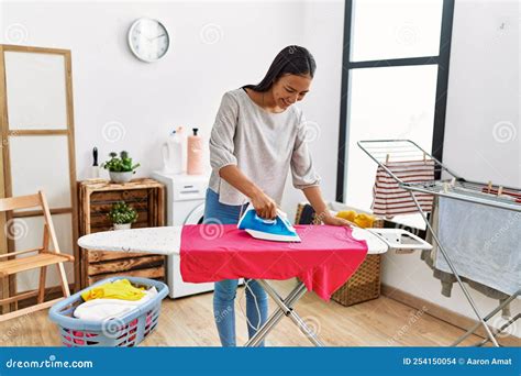 Young Latin Woman Smiling Confident Ironing At Laundry Room Stock Photo