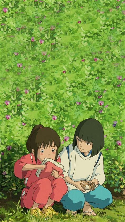 Two People Sitting On The Ground In Front Of Some Bushes And Flowers