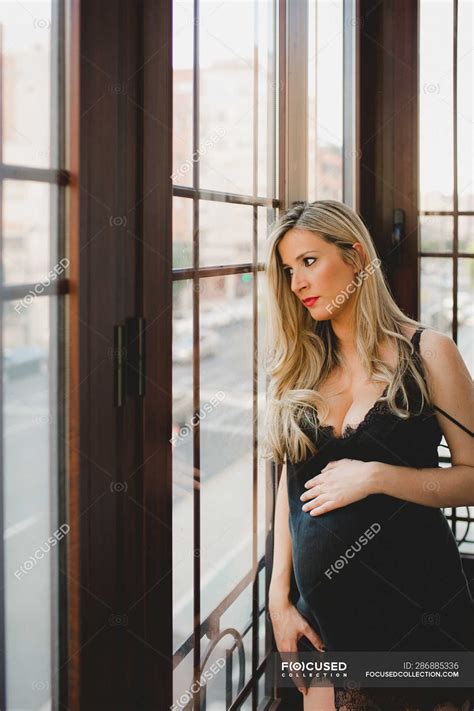 Thoughtful Pregnant Woman In Lingerie Standing Near Window At Home