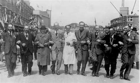 A Group Of People Walking Down A Street Next To Each Other