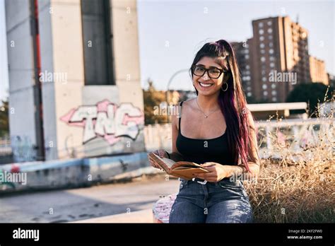 jeune femme latine brunette avec des lunettes lip perçage jeans cheveux longs assis dans un parc