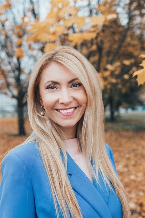 Smiling Blond Mature Woman Looking At Camera In Autumn Park Stock Photo
