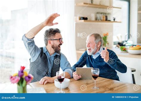 Adult Hipster Son And Senior Father Sitting At The Table Indoors At