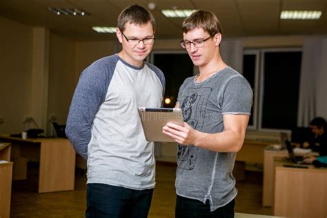 Two Young People Are Discussing A Project In The Office Standing Next To Each Other One Of