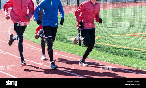 Four track and field athletes are running together on a red track ...