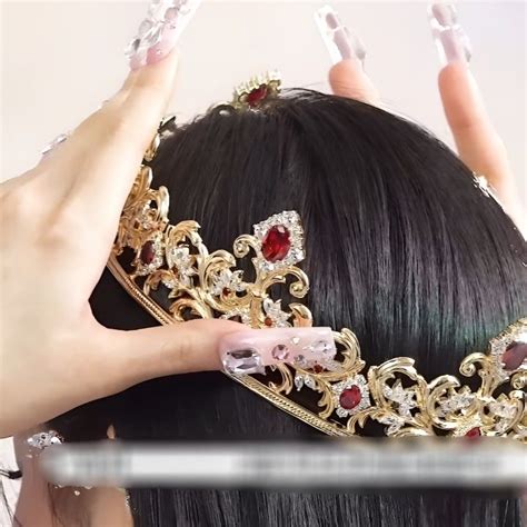 A Woman With Black Hair Wearing A Tiara And Holding Her Hands Up To Her Head