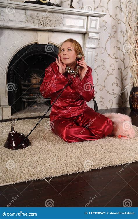 A Woman In Red Pajamas Is Sitting By The Marble Fireplace Talking On A