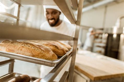 Happy African American Baker Looking At Fresh Loaves Of Bread Stock