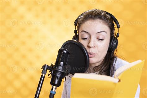 Woman wearing headphones reading aloud from book into microphone