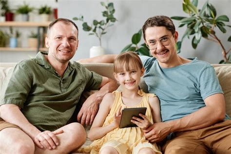 Retrato De Familia Gay Sentado En El Sof Con Hija Adoptiva Mediante Tableta Digital En Casa