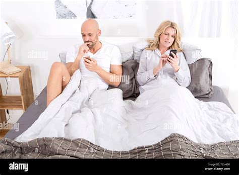Mature Couple Sitting In Bed Using Smartphones Stock Photo Alamy
