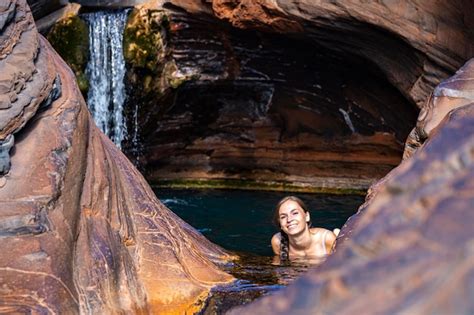Una Chica En Bikini Blanco Se Relaja En Una Piscina De Rocas Con Una Cascada Sobre Su Cabeza