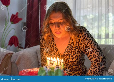 Pretty Blond Fashion Girl Blowing The Candles Of Her Birthday Cake Sitting In A Sofa Happy