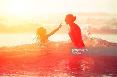 Mother And Daughter Jumping In Sea A Breaking Wave At Sunset Splash