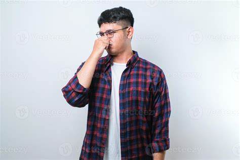 Young asian man smelling something stinky and disgusting, intolerable