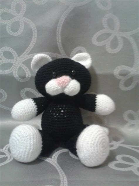 A Small Black And White Crocheted Teddy Bear Sitting On A Bed With An