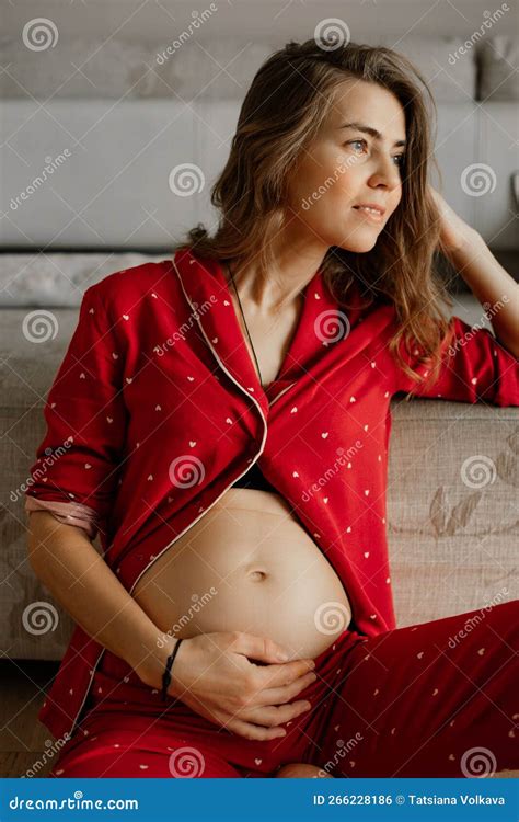 Vertical Calm Pensive Pregnant Blond Woman Sitting And Hold Naked Abdomen Wear Red Loose