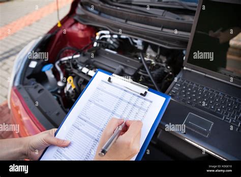 Male Mechanic Writing On Clipboard While Examining Car Engine Stock