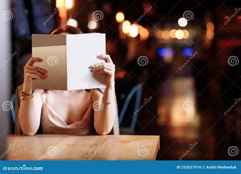 Beautiful Young Woman Is Holding And Covering Her Face Of Book With