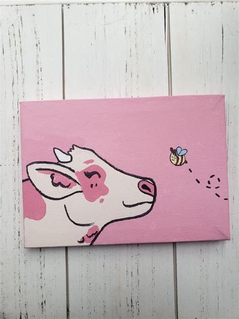 a painting of a cow with a bee on it's nose is hanging on a white wooden wall