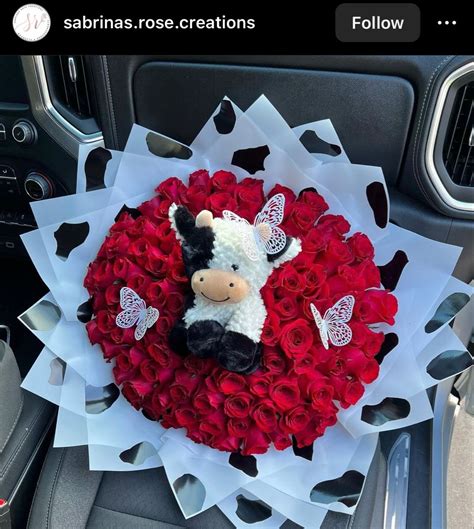 A Stuffed Cow Sitting In The Center Of A Bouquet Of Red Roses On Top Of