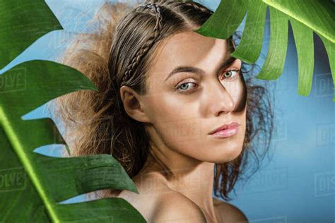 Portrait Of Confident Naked Woman With Palm Leaves Against Blue Sky